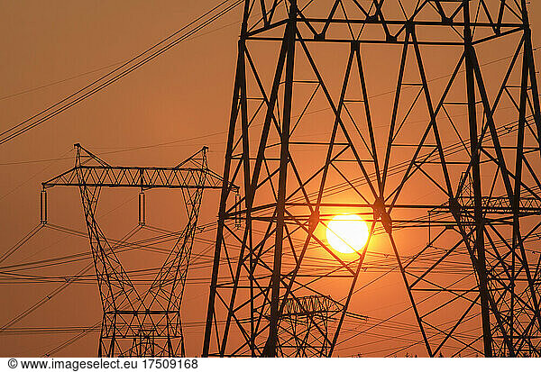 Strommast und Stromleitungen mit Sonne im Hintergrund.