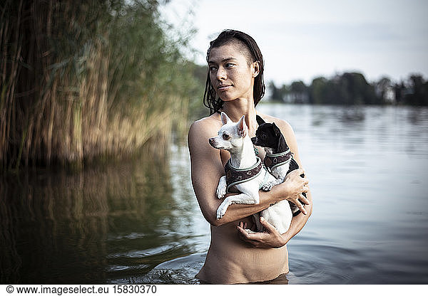 strong beautiful woman holds two small dogs in natural berlin lake