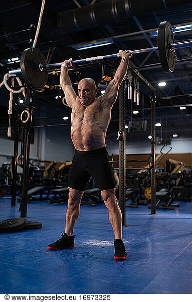 Strong elderly athlete with barbell over head