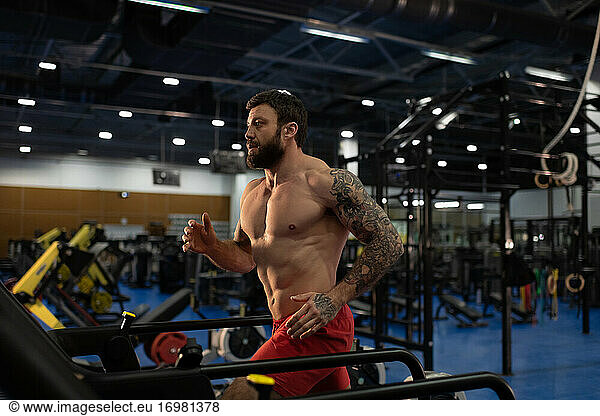 Strong male athlete running on modern treadmill