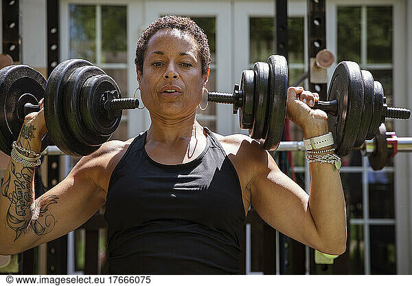 Strong mature woman weightlifting in sunny backyard