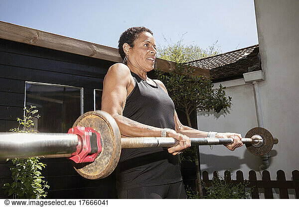 Strong mature woman weightlifting with barbell in backyard