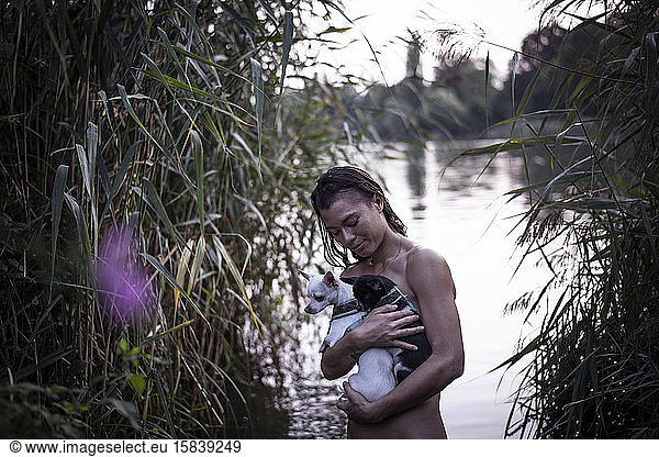 strong mixed race woman holds two small dogs in natural berlin lake