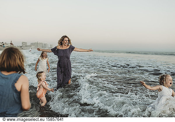 Strong mother with four daughters playing in ocean at sunset