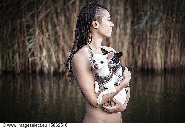 strong smiling woman holds two small dogs in natural berlin lake
