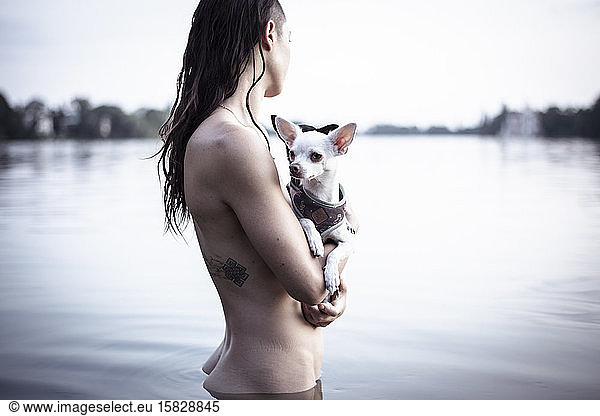 strong woman with tatoo holds two small dogs in natural berlin lake