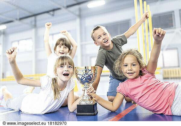 Students cheering with each other holding trophy at school sports court