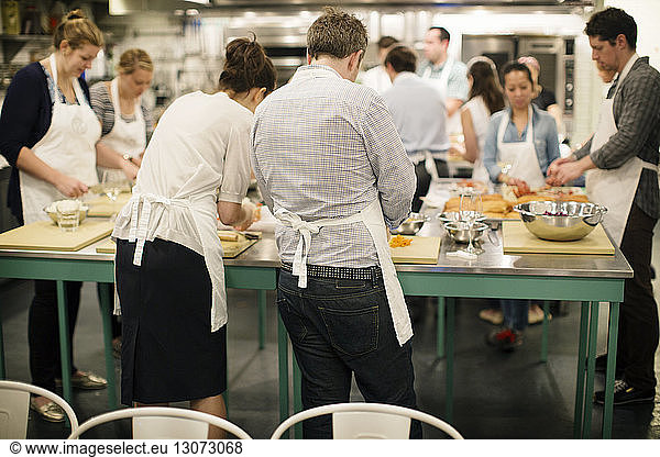 Students preparing food at tables while standing at commercial kitchen