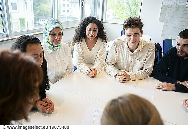 Students sitting with hands clasped around table in classroom