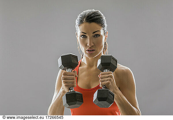 Studio portrait of athletic woman in red sleeveless top with dumbbells