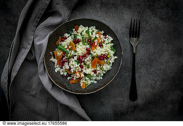 Studio shot of bowl of cauliflower salad with apricot  pomegranate seeds  pistachios  mint and parsley