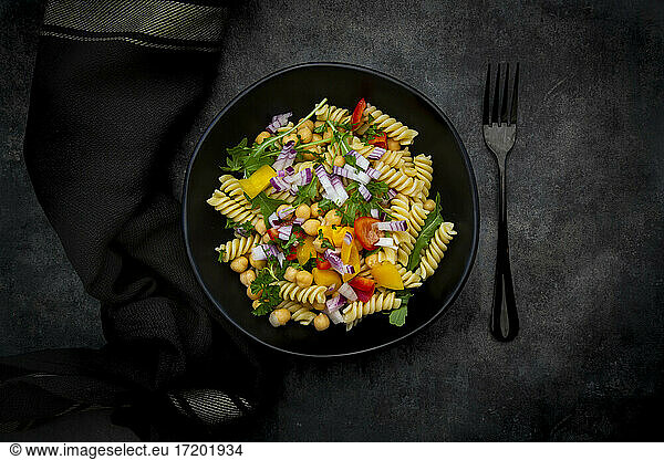 Studio shot of bowl of fusilli pasta salad with chick-peas  bell peppers  arugula  Spanish onion  basil and parsley