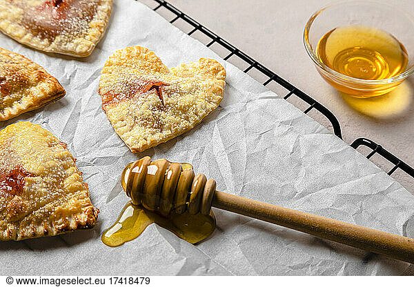 Studio shot of bowl of honey  honey dipper and freshly baked heart shaped mini pies