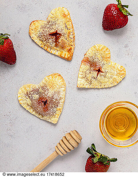 Studio shot of bowl of honey  honey dipper  strawberries and freshly baked heart shaped mini pies