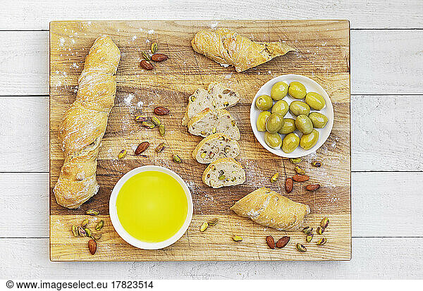 Studio shot of bowl of olive oil  green olives and loaves of homemade Pain Paillasse bread with almonds and pistachios