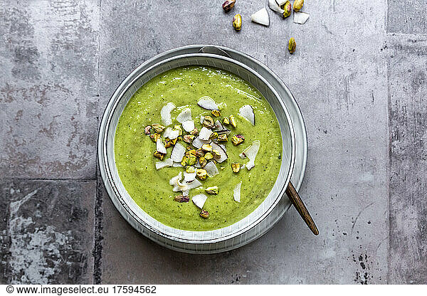 Studio shot of bowl of vegan pea soup with zucchini  broccoli  pistachios and coconut shreds