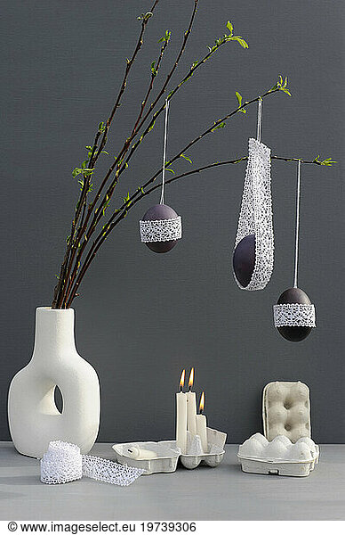 Studio shot of candles burning under laced Easter eggs hanging from twigs in vase