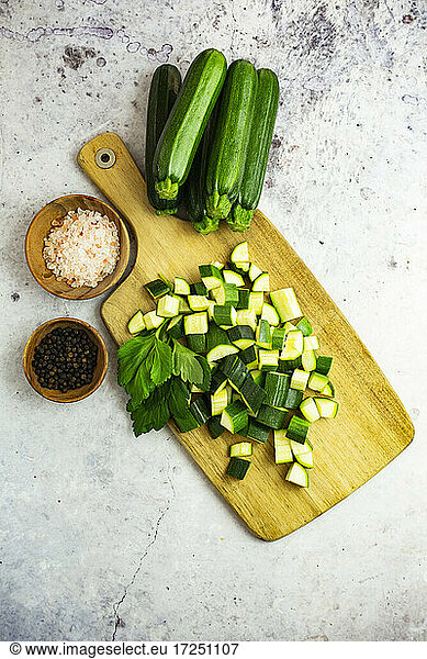 Studio shot of chopped parsley and zucchinis and wooden bowls with black peppercorns and Himalayan salt