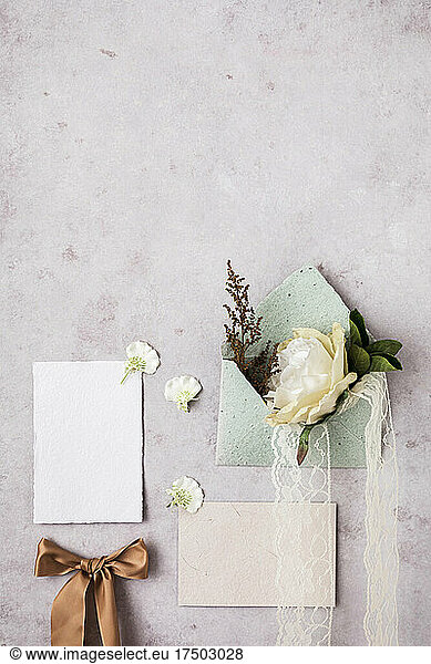 Studio shot of envelope  invitation card  tied bow and flowers flat laid against light pink background