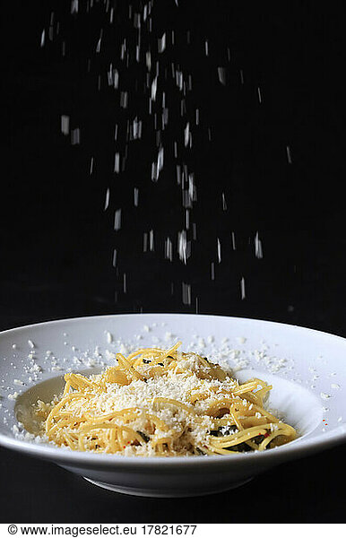 Studio shot of grated Parmesan pouring on plate of pasta