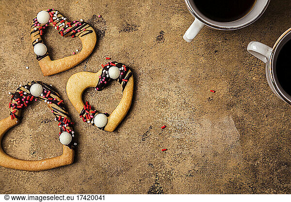 Studio shot of heart shaped cookies and two cups of coffee standing against brown background