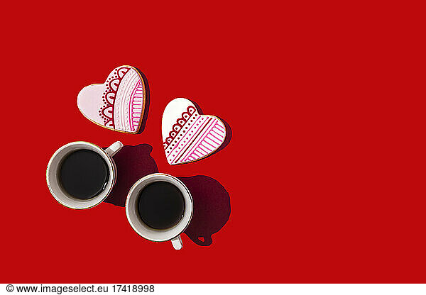 Studio shot of heart shaped cookies and two cups of coffee standing against red background