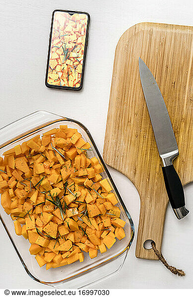 Studio shot of kitchen knife  cutting board  smart phone and glass baking pan filled with chopped squash