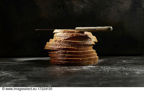 Studio shot of kitchen knife lying on top of stack of fresh bread slices