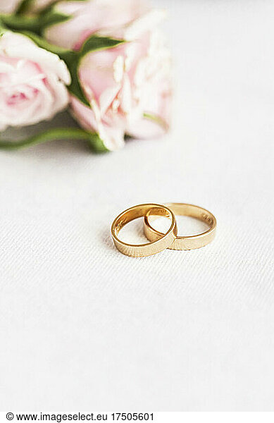 Studio shot of pair of golden wedding rings with roses in background
