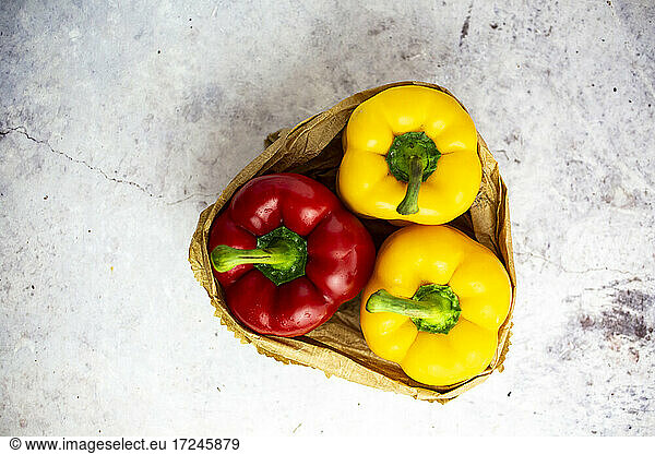 Studio shot of paper bag with single red and two yellow bell peppers