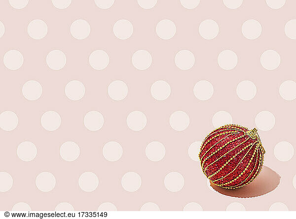 Studio shot of red Christmas ornament lying against pink polka dot background