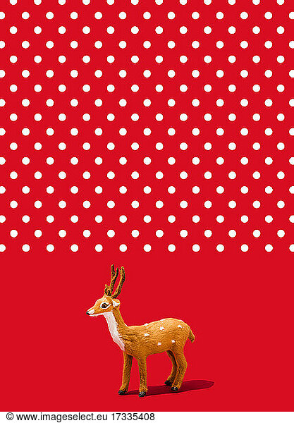 Studio shot of reindeer figurine standing against vibrant red polka dot background