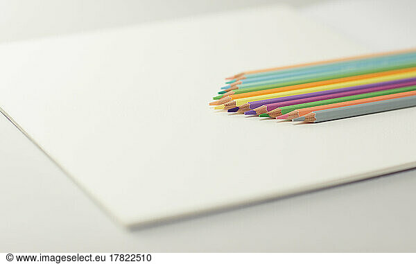 Studio shot of row of colored pencils lying on top of drawing paper block
