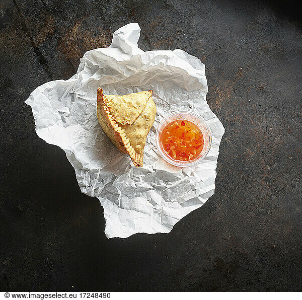 Studio shot of samosa dumpling and bowl of chili sauce on paper napkin