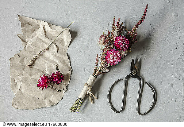 Studio shot of scissors  piece of paper and small bouquet of dried flowers