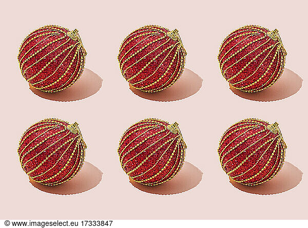 Studio shot of six red Christmas ornaments lying against pink background