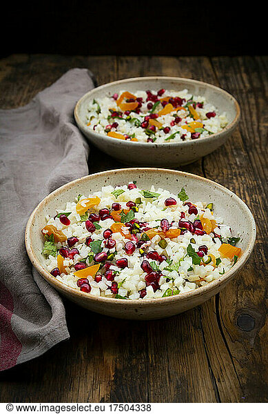 Studio shot of two bowls of cauliflower salad with pomegranate seeds  pistachios  mint  parsley and apricot