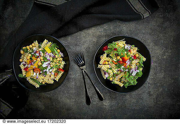 Studio shot of two bowls of fusilli pasta salad with chick-peas  bell peppers  arugula  Spanish onion  basil and parsley