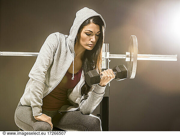 Studio shot of woman in hooded shirt exercising with dumbbell