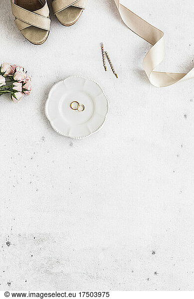 Studio shot of women's shoes, roses, ribbon and plate with pair of wedding rings