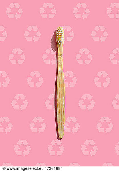Studio shot of wooden toothbrush lying against pink pattern with recycling symbols