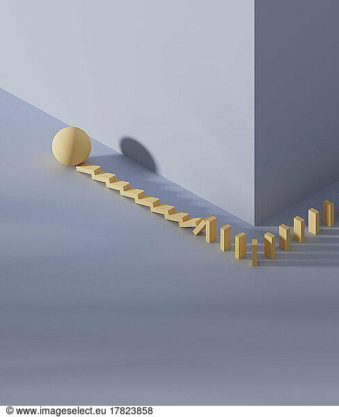 Studio shot of yellow sphere knocking down domino pieces placed around corner