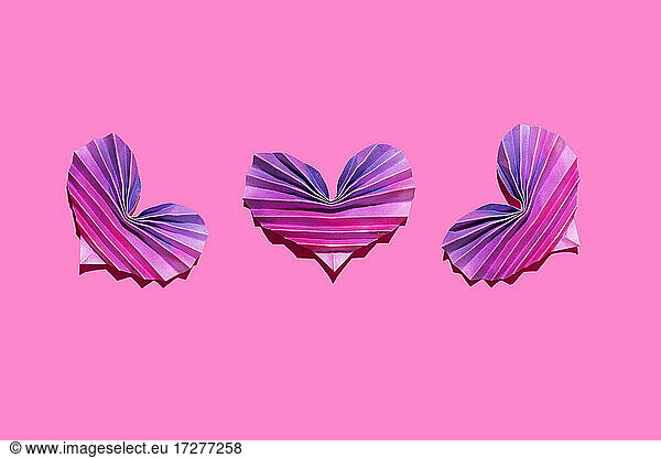 Studioaufnahme von drei rosa und lila Origami-Herzen