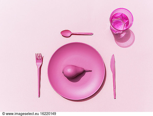 Studioaufnahme von rosa Plastikteller  Plastikbesteck  Glas Wasser und rosa Birne