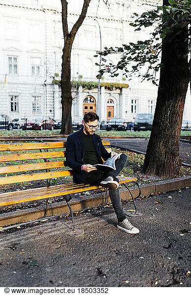 Stylish curly man reading a book while sitting in the park