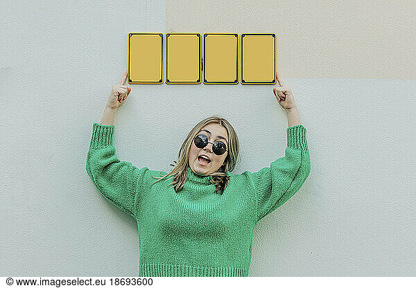 Stylish girl in green sweater holding nameplates on wall
