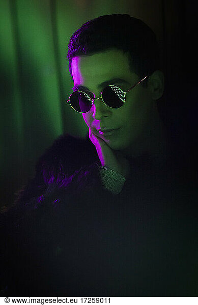 Stylish young man wearing sunglasses in dark
