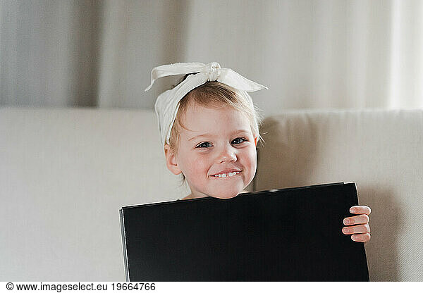 Stylishly dressed girl 2 years old hugs a huge fashion book  laughs