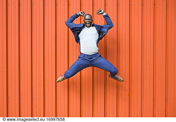 Successfull businessman jumping in the air in front of orange wall screaming