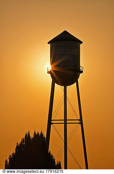 Sun setting behind agricultural water tower.